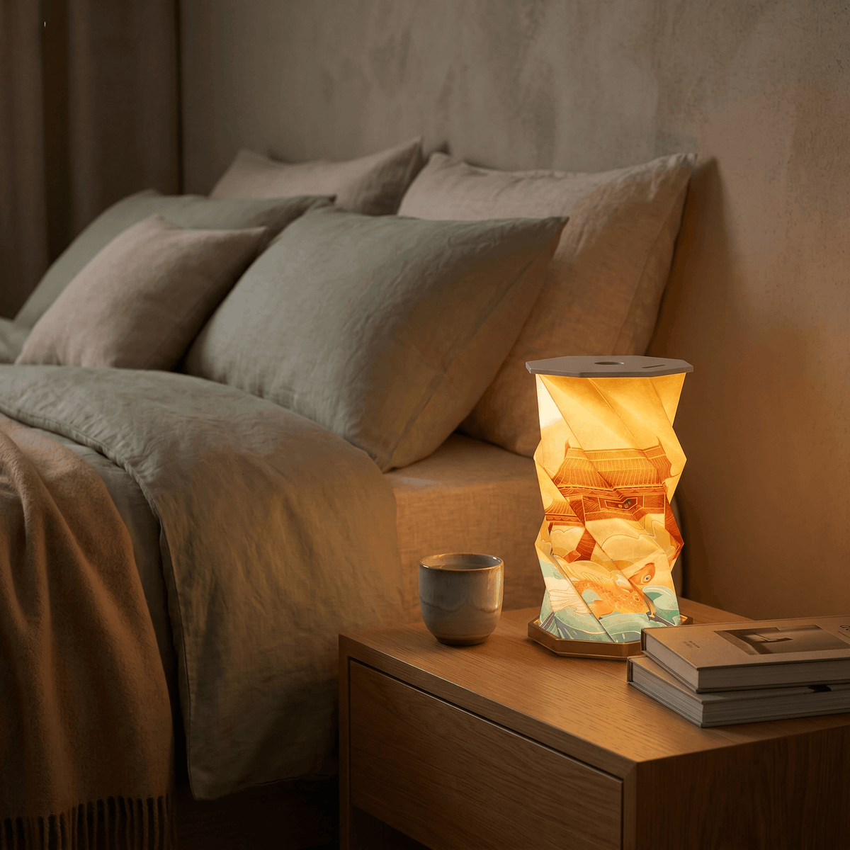 Lanterne OrigaLux allumée sur une table de chevet dans une chambre chaleureuse.